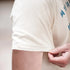 Close-up of a person wearing a white t-shirt with text on it, holding their arm.